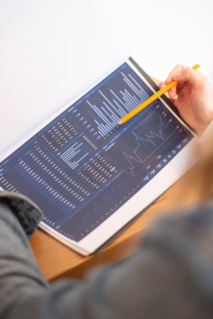 A close-up of a person analyzing blue graph data with a yellow pencil.